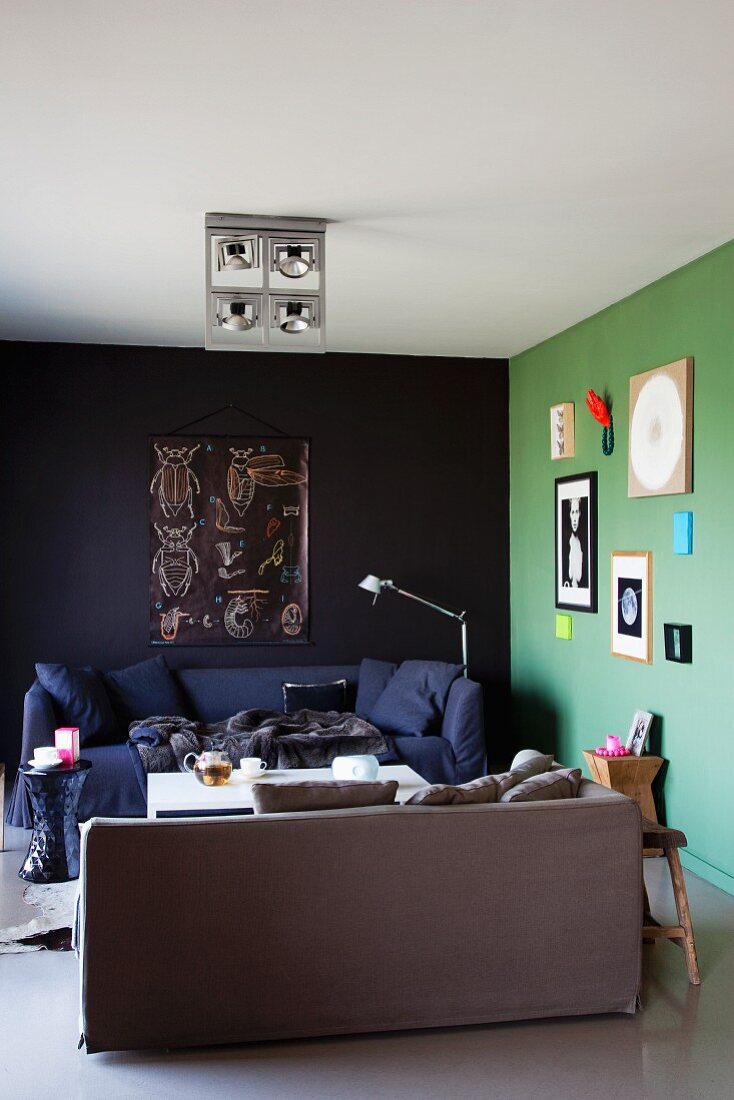 Mit Bildern künstlerisch dekorierte lindgrüne Wand neben schwarzer Wand und zwei gemütlichen Polstersofas in Appartementecke