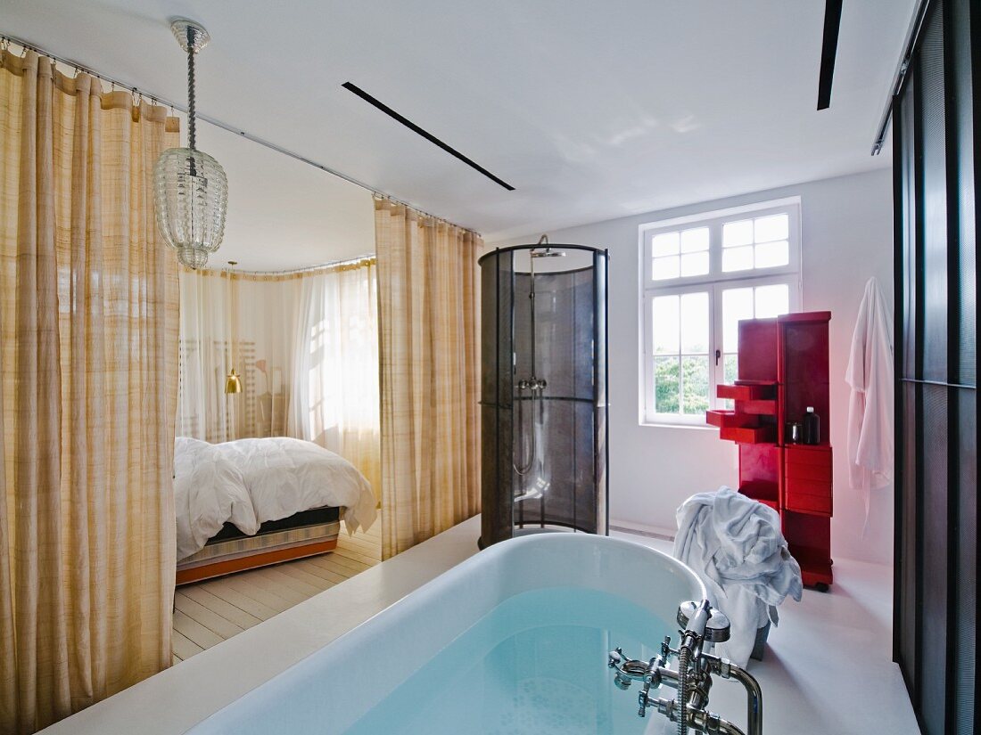 Free-standing bathtub in ensuite bathroom with view into bedroom through open curtains