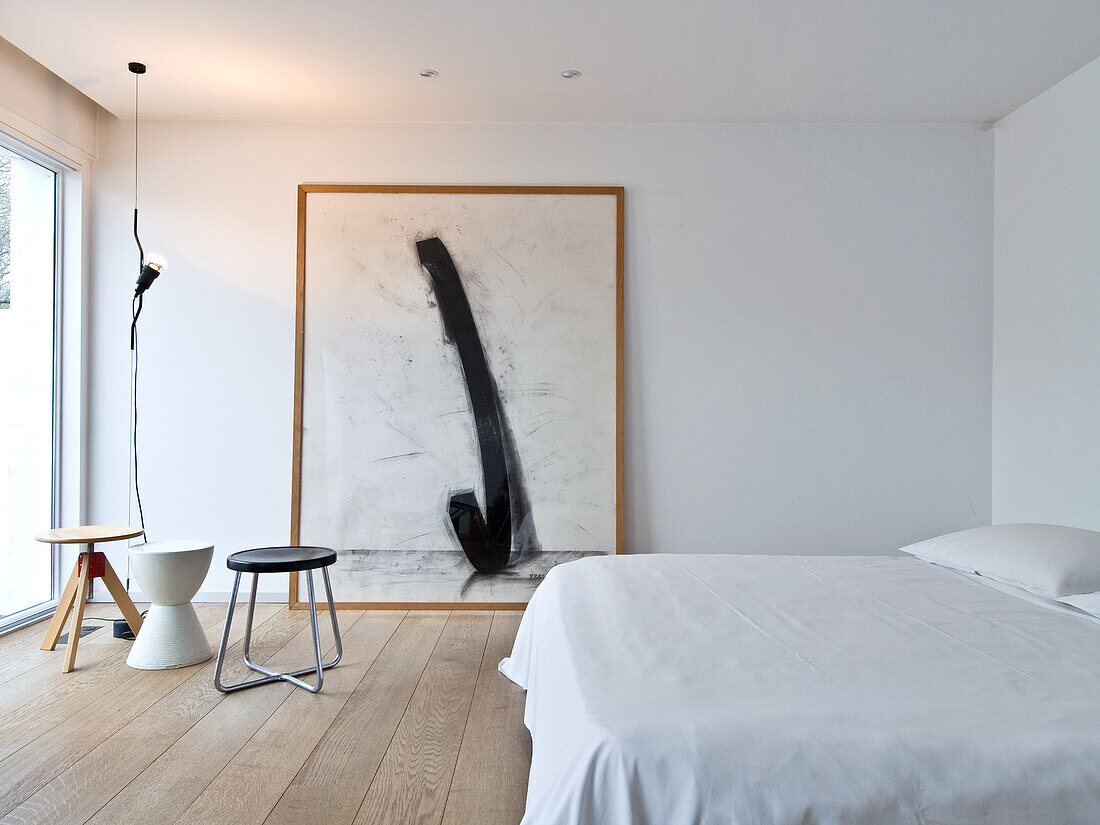 Minimalist bedroom with large abstract painting and white bed linen