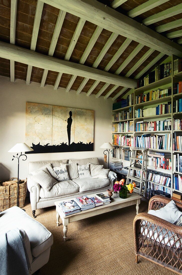 Comfortable living room with country-style seating area and bookcase below rustic wood-beamed ceiling
