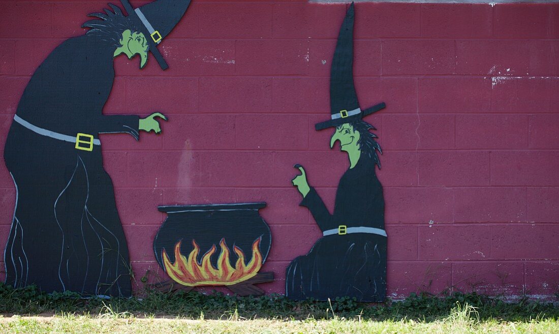 Hexenfiguren mit Kessel an einer Wand im Garten für Halloween