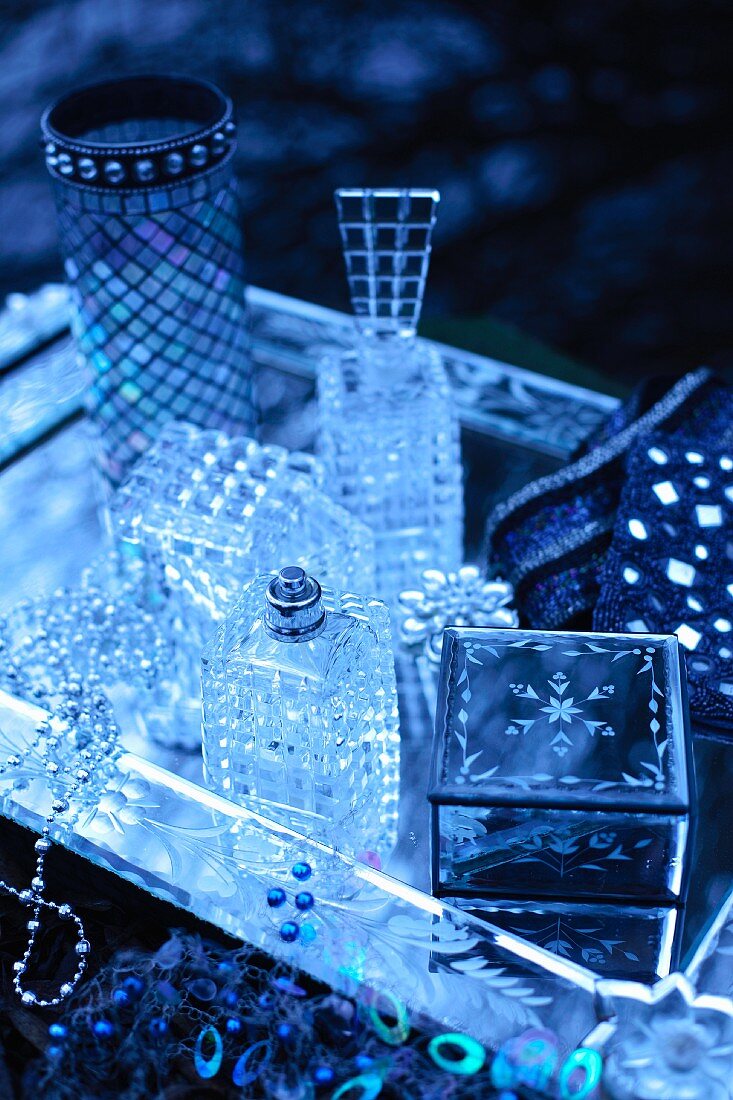 Stillleben mit Schmuckkästchen, Parfumflakons und Vase auf Silbertablett in bläulichem Licht