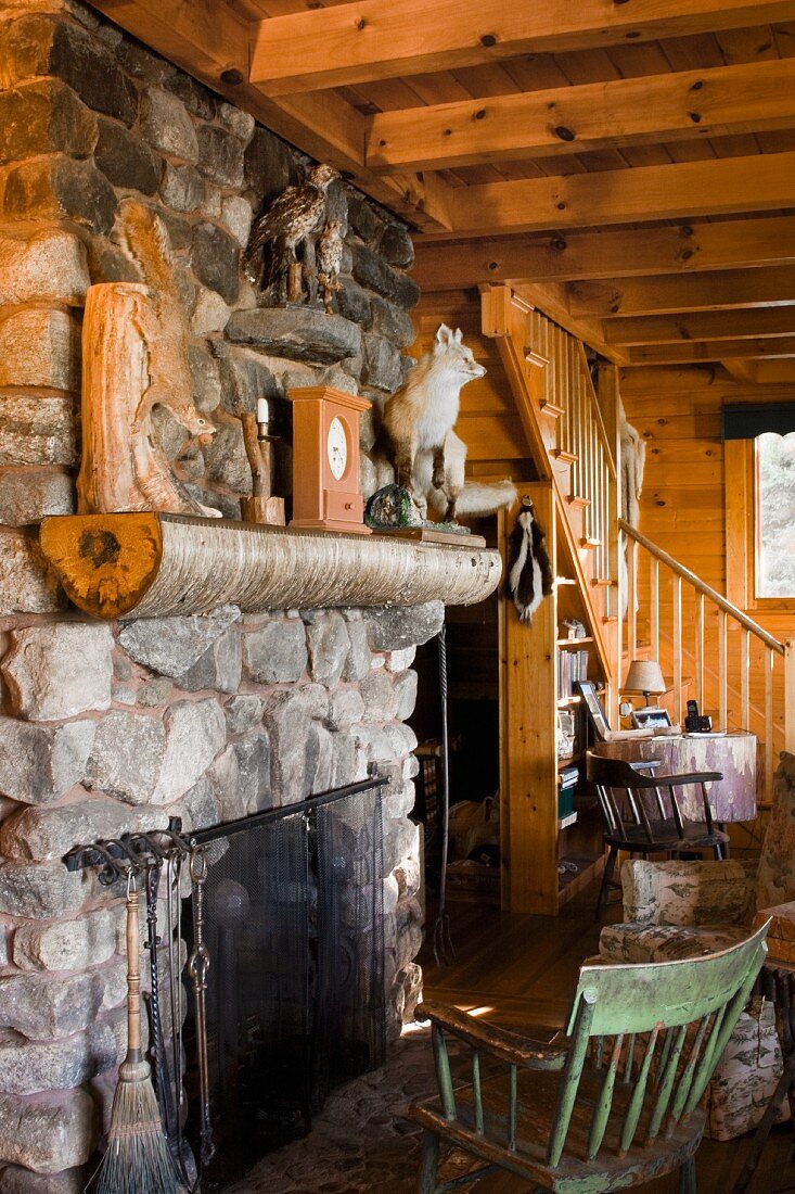 Holzstuhl vor Natursteinkamin Kamin und Tiertrophäen auf dem Sims in rustikaler Hütte