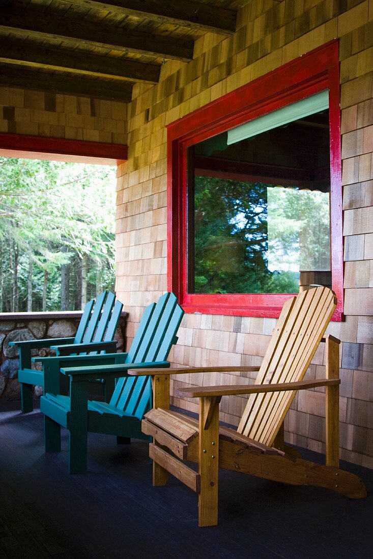 Adirondack-Stühle auf der Veranda, teilweise blau bemalt, vor Schindelwand und Fenster mit rot lackiertem Rahmen
