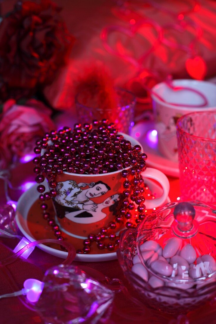 String of red beads in teacup next to glass bonbonniere on red velvet cloth