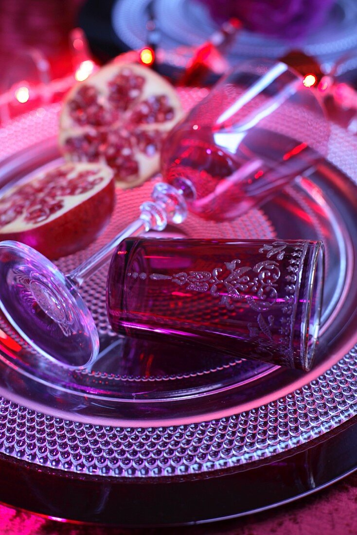 Still-life arrangement of stemmed glass and Oriental tea glass next to cut pomegranate on platter