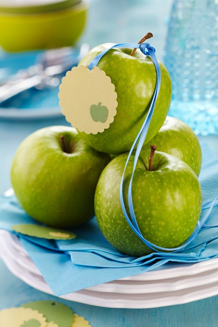 Grüne Äpfel mit Satinband und Anhänger auf Tellerstapel