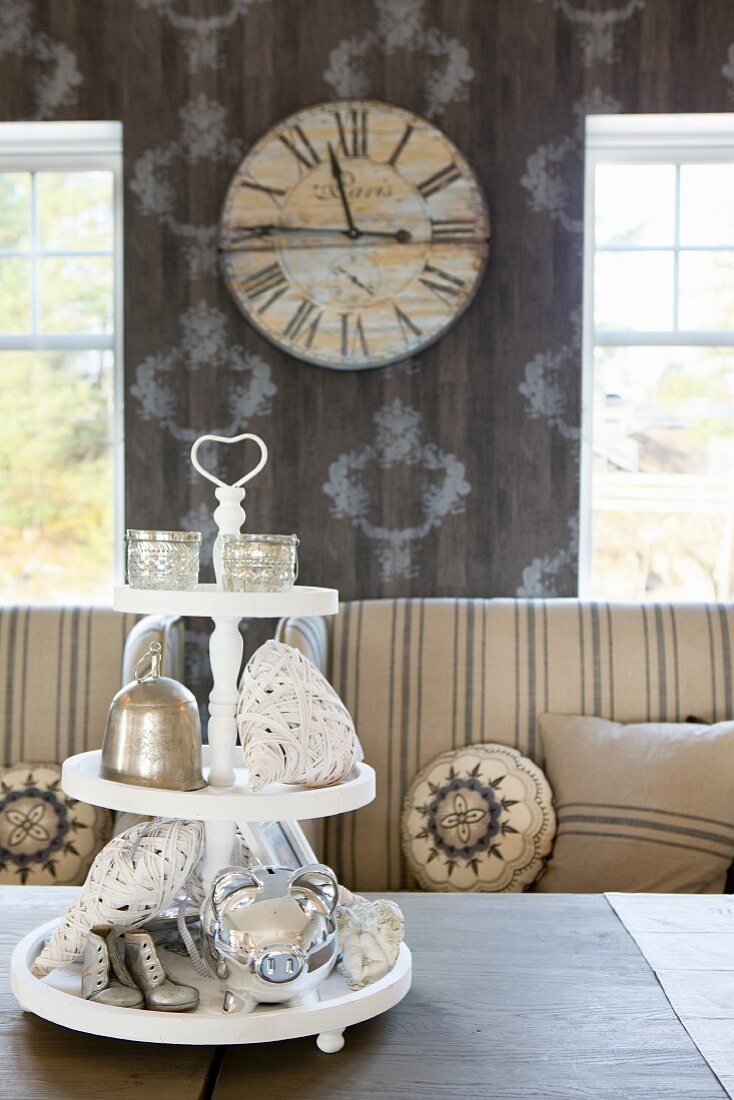 Silverware on white cake stand in front of striped sofas with round scatter cushions and nostalgic wall clock