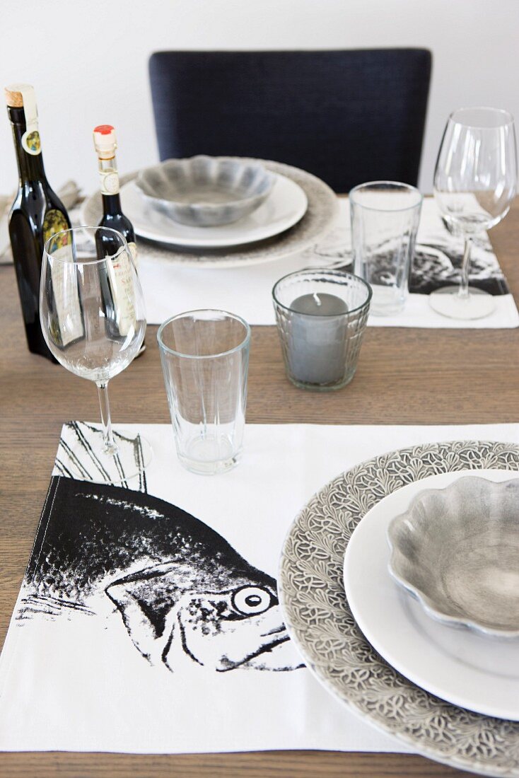 Table settings with grey plates on black and white placemats with fish motifs