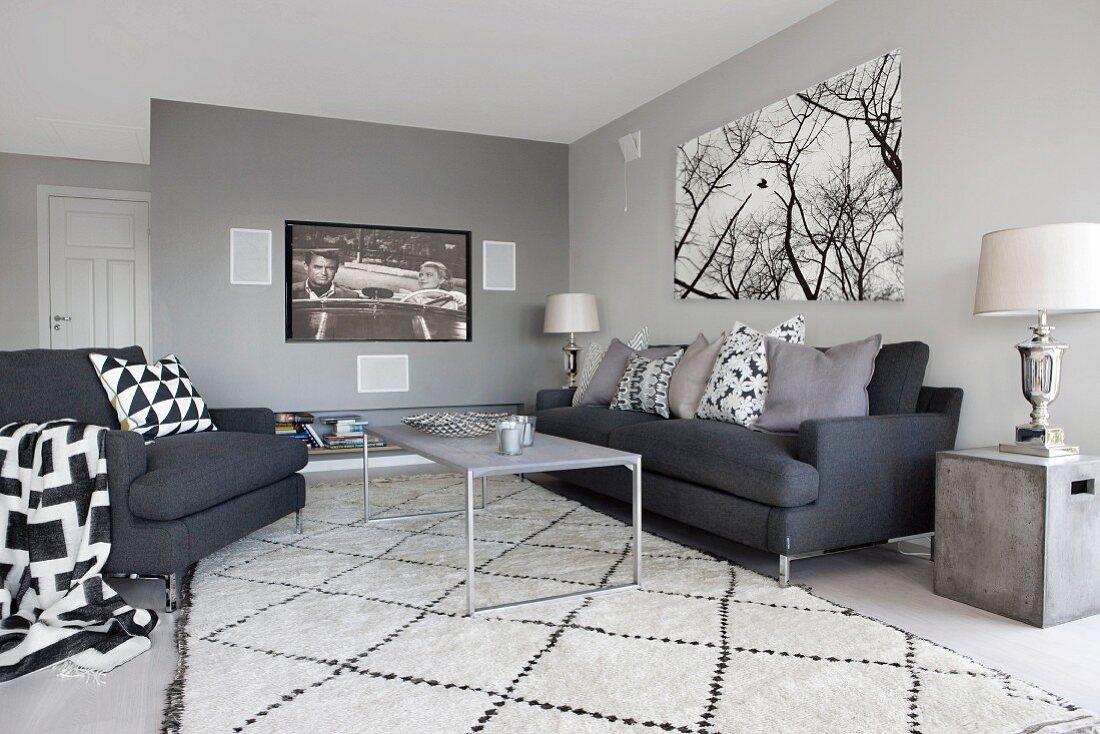 Anthrazitfarbene Sitzgruppe mit schwarzweissen Kissen und Teppich; Flatscreen und Bild mit Baummotiv an der Wand