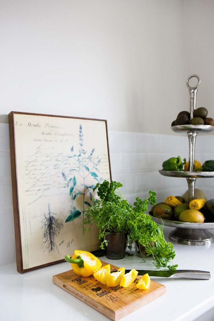 Yellow pepper cut open on wooden chopping board, parsley and cake stand of vegetables in front of old botanical illustration