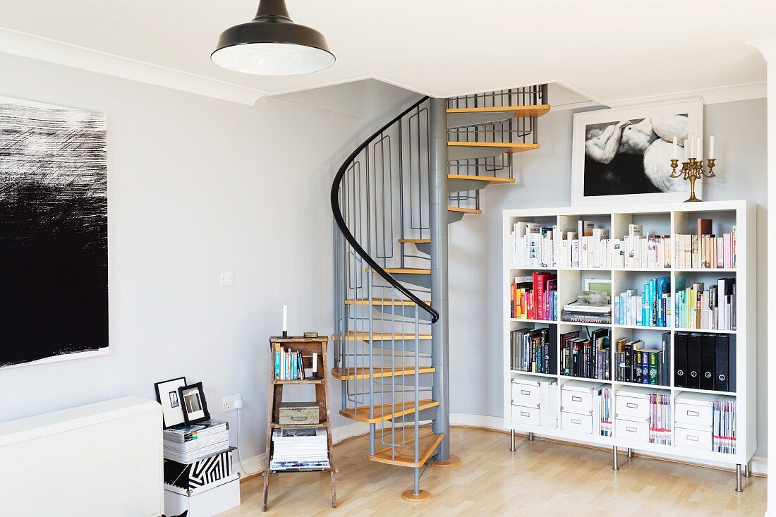 Corner of living room with bookcase and spiral staircase leading to mezzanine in English loft apartment in converted factory
