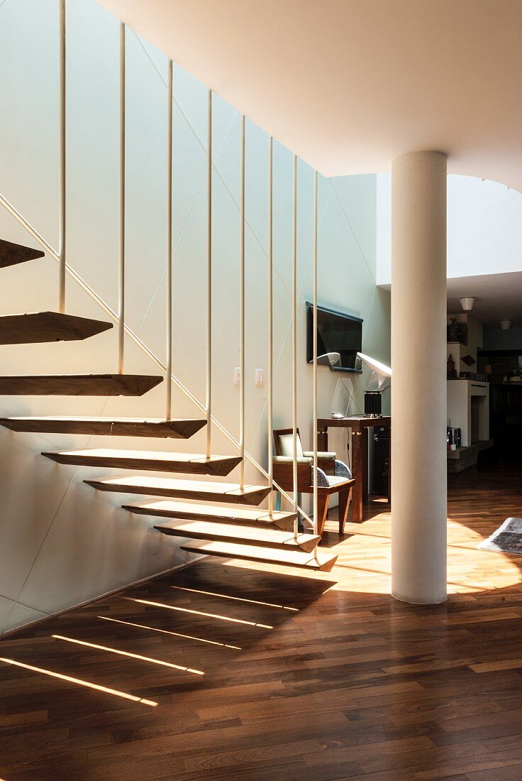 Pattern of light and shade cast by airy, floating stair treads attached to baluster rods below mezzanine level