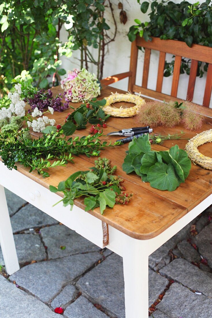 Gartentisch mit Blumenschere, frisch geschnittenen Blüten, Zweigen und Strohkränzen