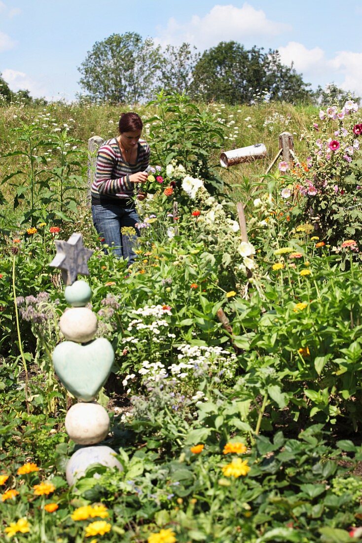 Frau beim Blumenschneiden in üppigem Bauerngarten