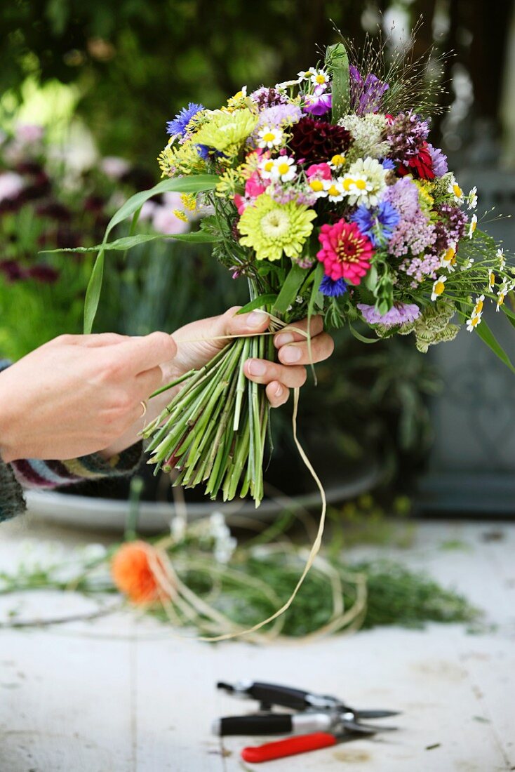 Floristenhände beim Binden eines sommerlichen Blumenstrausses