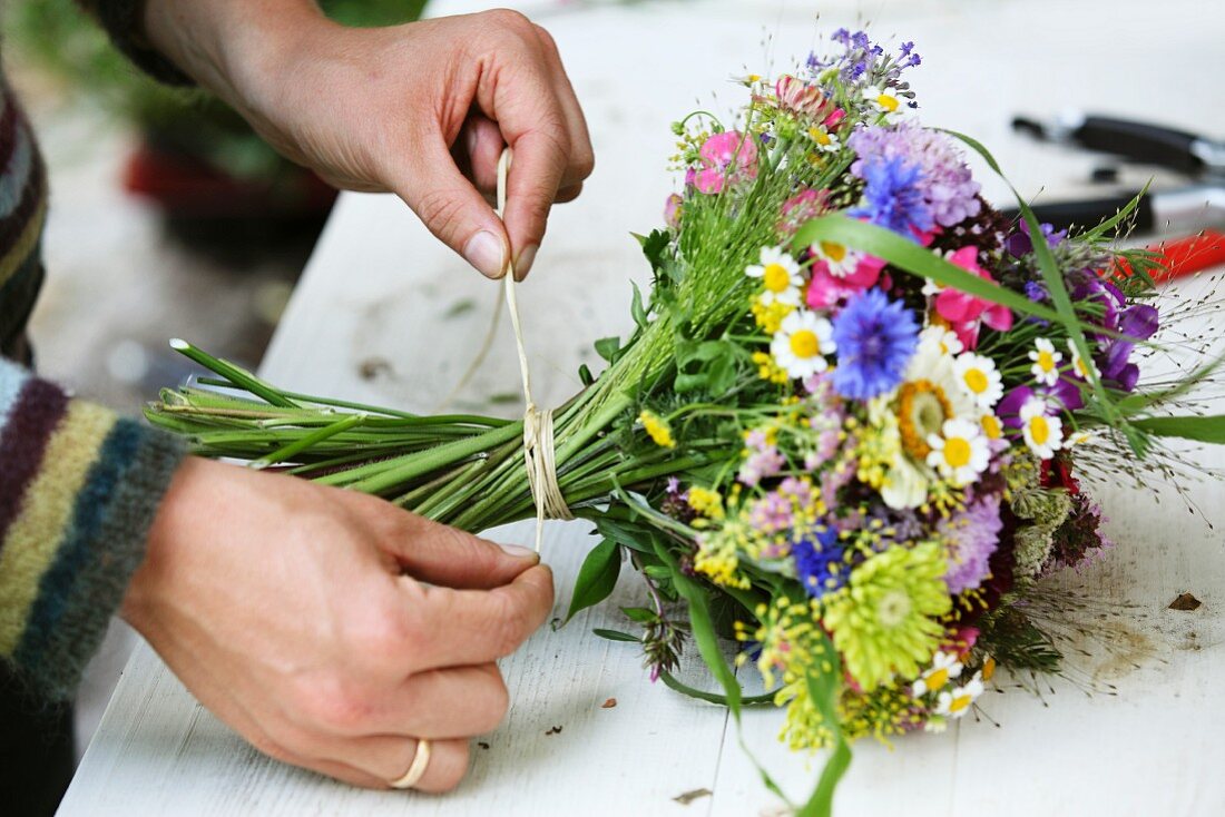 Floristenhände beim Binden eines sommerlichen Blumenstrausses