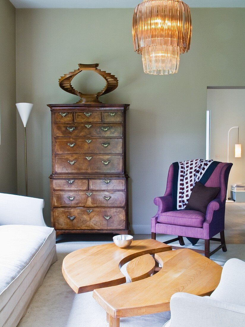 Wohnraum im Stilmix mit Designer-Couchtisch, antikem Wandschrank & lilafarbenem Postersessel