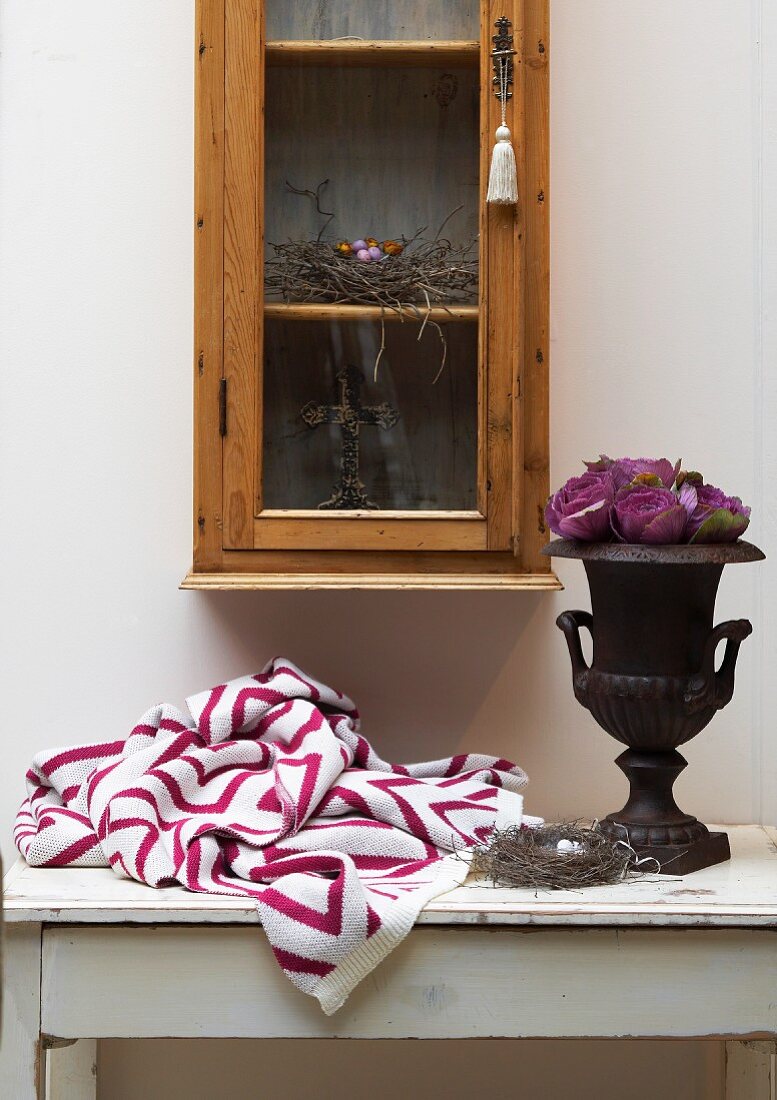 Knitted blanket with graphic pattern and roses in urn on vintage table below glass-fronted cabinet