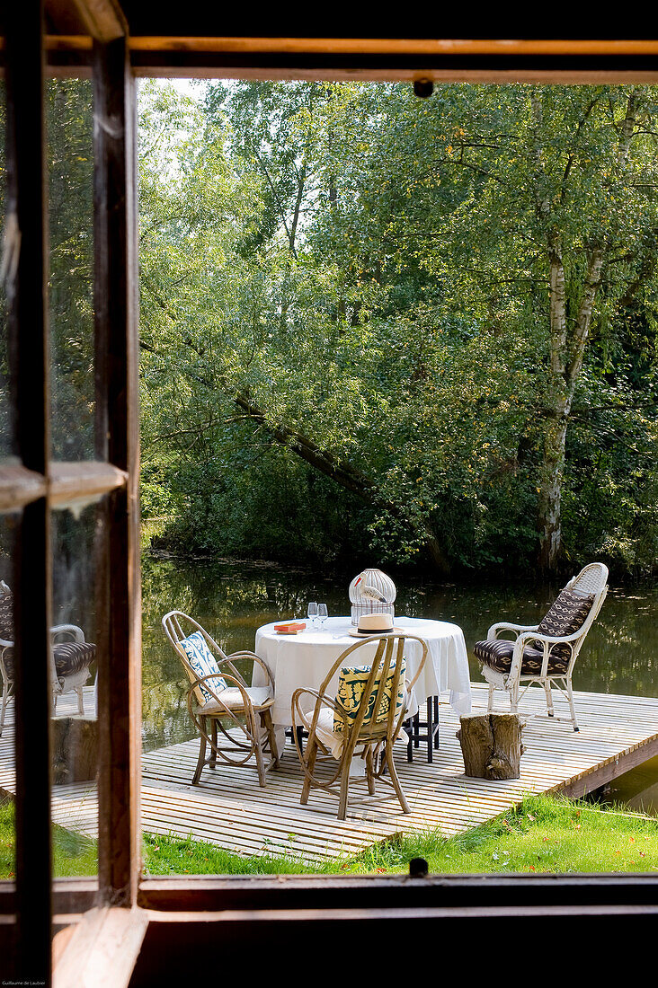 Set table and chairs on wooden dock by the water, surrounded by greenery