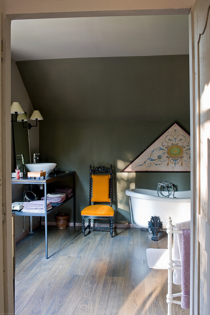 Bathroom with free-standing bathtub and antique chair on wooden floorboards