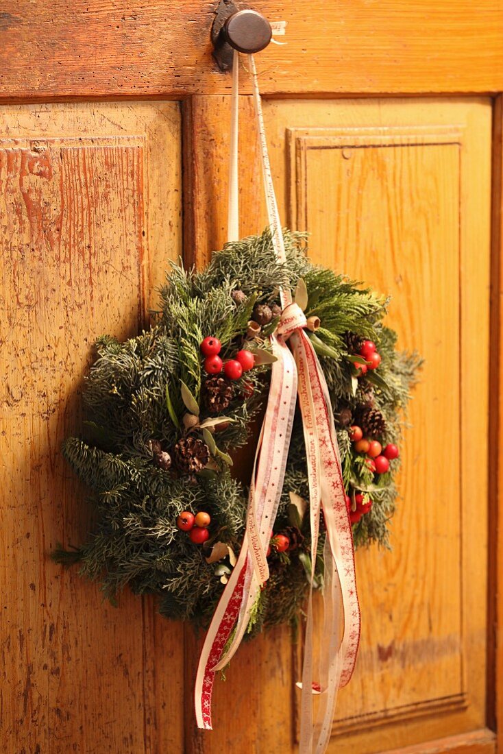 Weihnachtlicher Kranz mit Beeren und Bändern an einer Schranktür