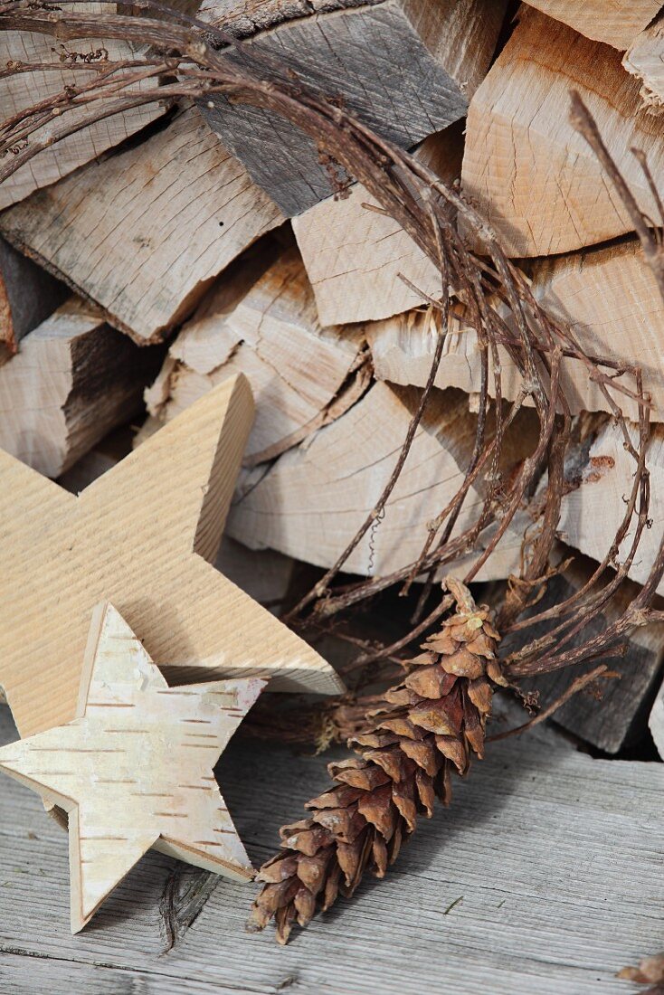Holzsterne und Tannenzapfen vor gelagerten Holzscheiten - weihnachtlich im Vintage Ambiente