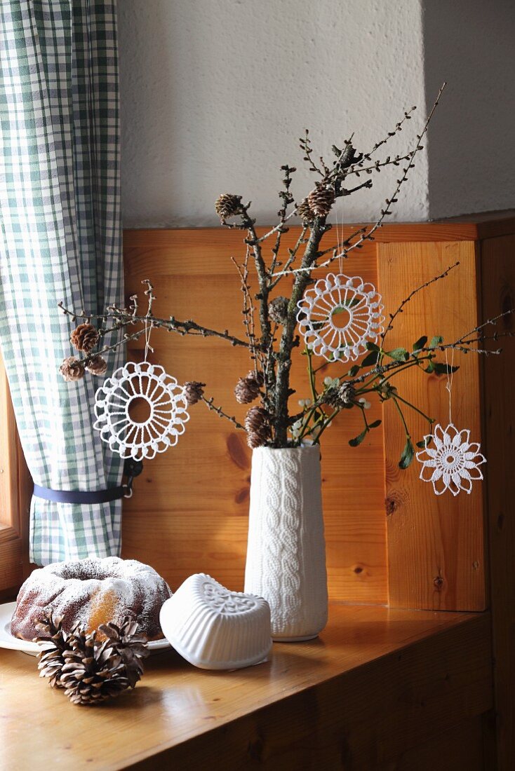 White, crocheted stars hanging from gnarled branch and bundt cake on wood-panelled cabin windowsill