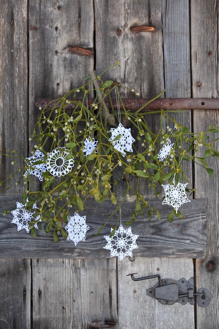 Nostalgic Christmas arrangement of ornate, white crocheted stars and branch of mistletoe on rustic, weathered wooden door