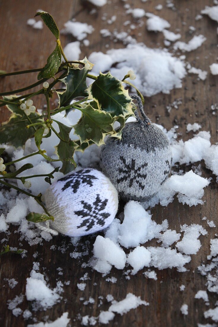 Knitted baubles with Norwegian pattern on wooden surface with snow and sprigs of mistletoe