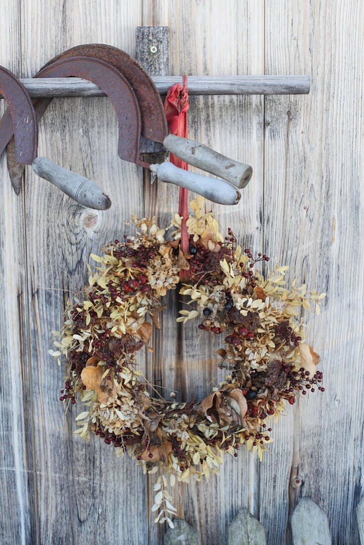 Herbstlicher Türkranz mit Beerenzweigen unter rostigen Sicheln an Holzstange aufgehängt