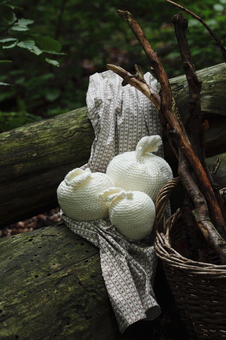 Crocheted apples of various sizes and wicker basket on tree trunk