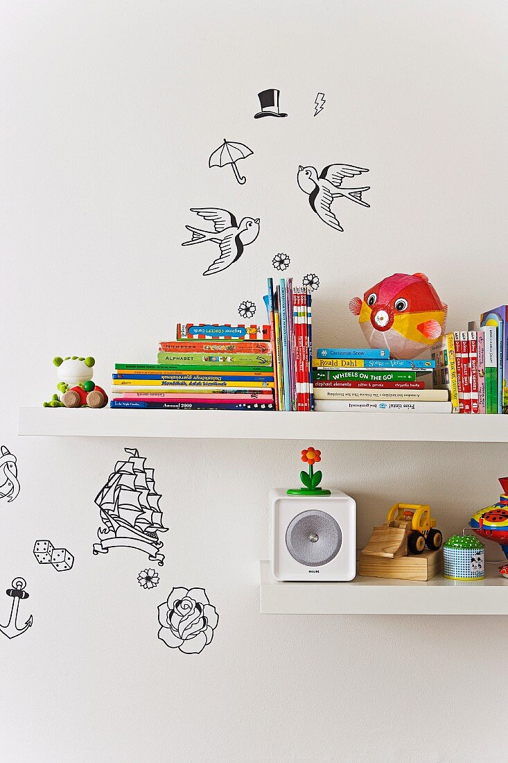 Ausschnitt von weissen Wandbords mit Kinderbüchern und Spielzeug, verschiedene Deko-Applikationen an Wand