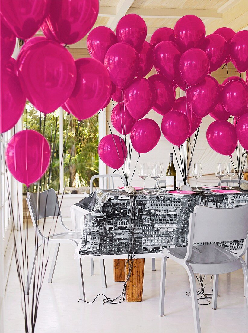 Hellgrau lackierte Stühle um dekorierten Tisch mit violetten Luftballons