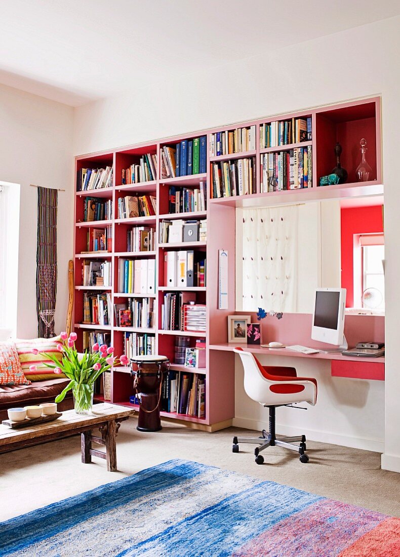 Pinkfarbenes Bücherregal mit integriertem Schreibplatz in einem Wohnzimmer