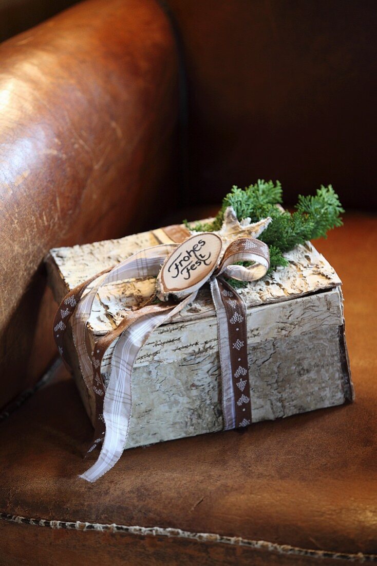 Kleines, weihnachtlich dekoriertes Paket aus Birkenrinde mit Geschenkband auf Ledersessel