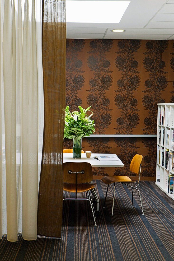 Bauhaus chairs at white table on striped rug, bronze wallpaper with dark floral pattern and floor-length curtains to one side