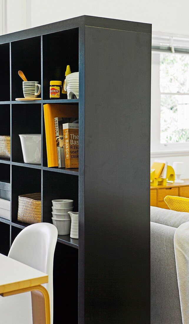 Schwarzes Regal als Raumteiler mit Stauraum für Geschirr und Bücher zwischen Essplatz und Loungebereich