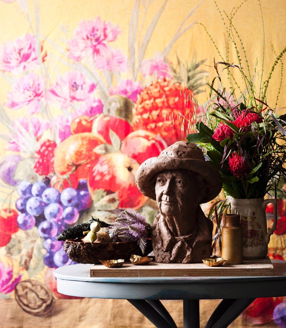 Kleine Büste und Blumenstrauss auf rundem Tisch vor Wandbehang mit Blumenmotiv