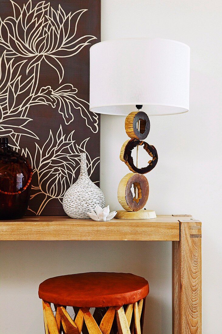 Tischleuchte mit künstlerich gestaltetenm Lampenfuss aus Baumstammscheiben und weisser Schirm auf Holztisch