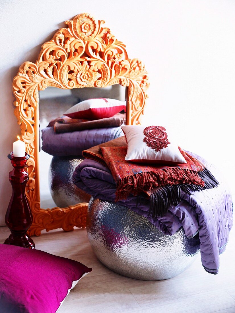 Kunstvoll geschnitzter Spiegelrahmen mit silberfarbener Kugelvase, gefalteten lilafarbenen Seidenschals und Dekokissen dekoriert