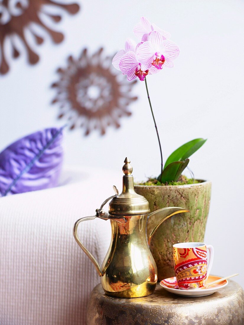 Red china cup, shiny brass jug and pink orchid in gold-coloured pot