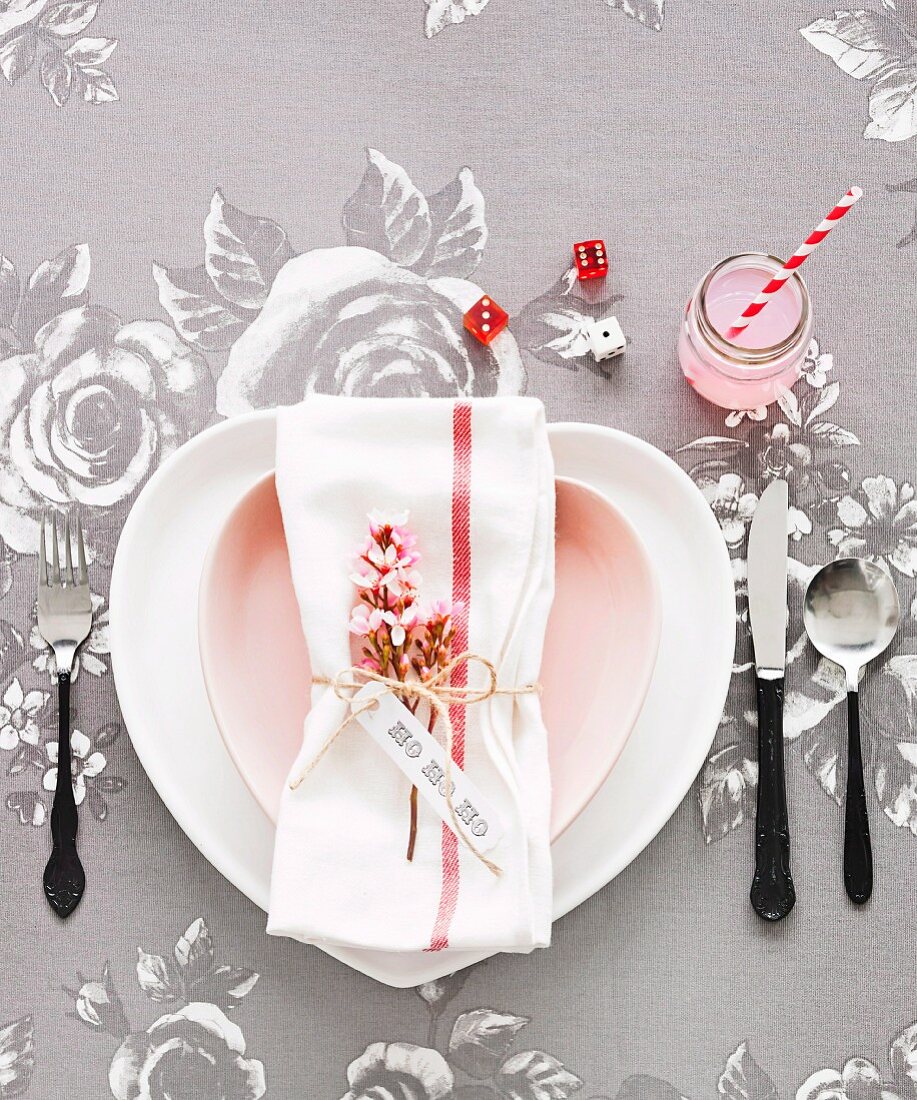 Romantic place setting with rose-patterned tablecloth, heart-shaped plate and sprig of pink flowers