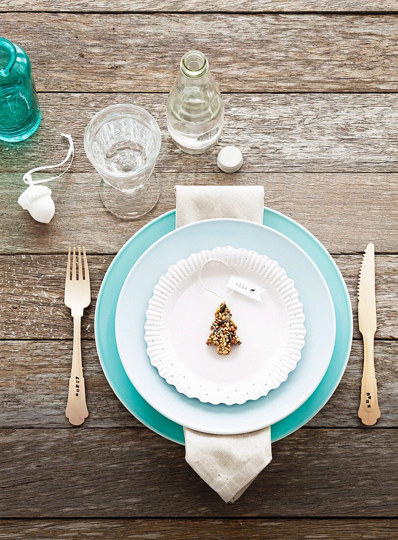 Hellblaues Gedeck mit Silberbesteck und Weihnachtsbaum-Keks dekoriert auf rustikalem verwittertem Holztisch