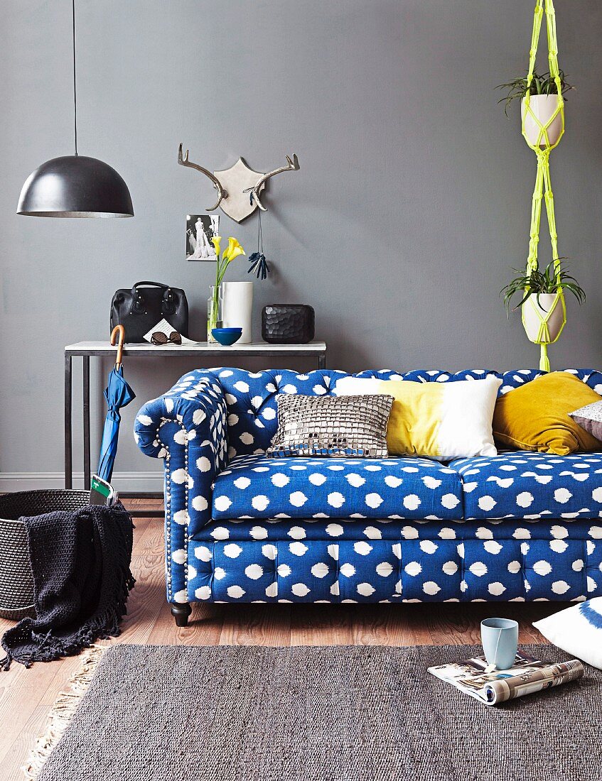 Blue and white polka-dot sofa in front of console table against grey wall and yellow macrame plant hanger