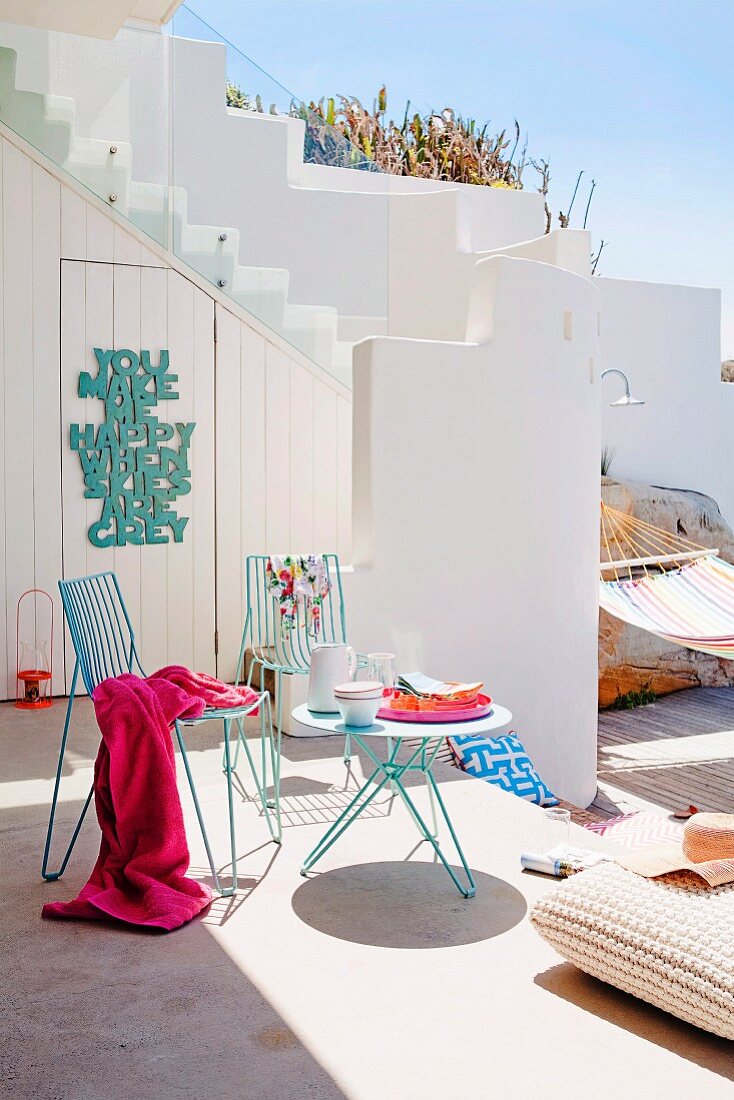 Terrassenbereich eines mediterranen weissen Wohnhauses mit Tisch & Stühlen aus Metall, Bodenkissen & Hängematte