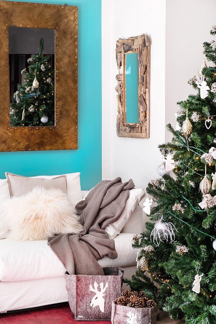 Geschmückter Weihnachtsbaum, helle Couch und Spiegel an blauer Wand im Wohnzimmer