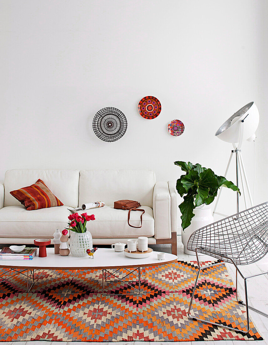 White upholstered sofa and wire mesh chair around classic coffee table on folkloric carpet