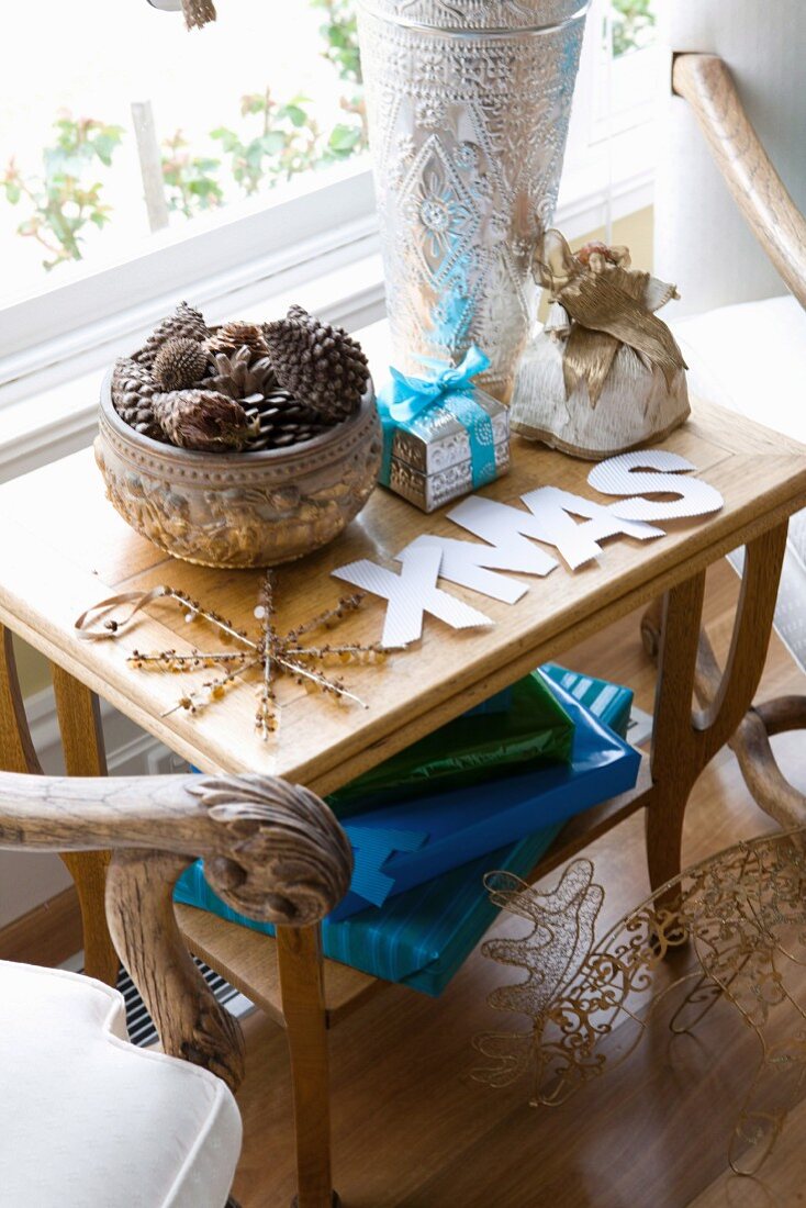 Elegant verpackte Geschenke neben Schale mit Zapfensammlung und XMAS-Buchstaben