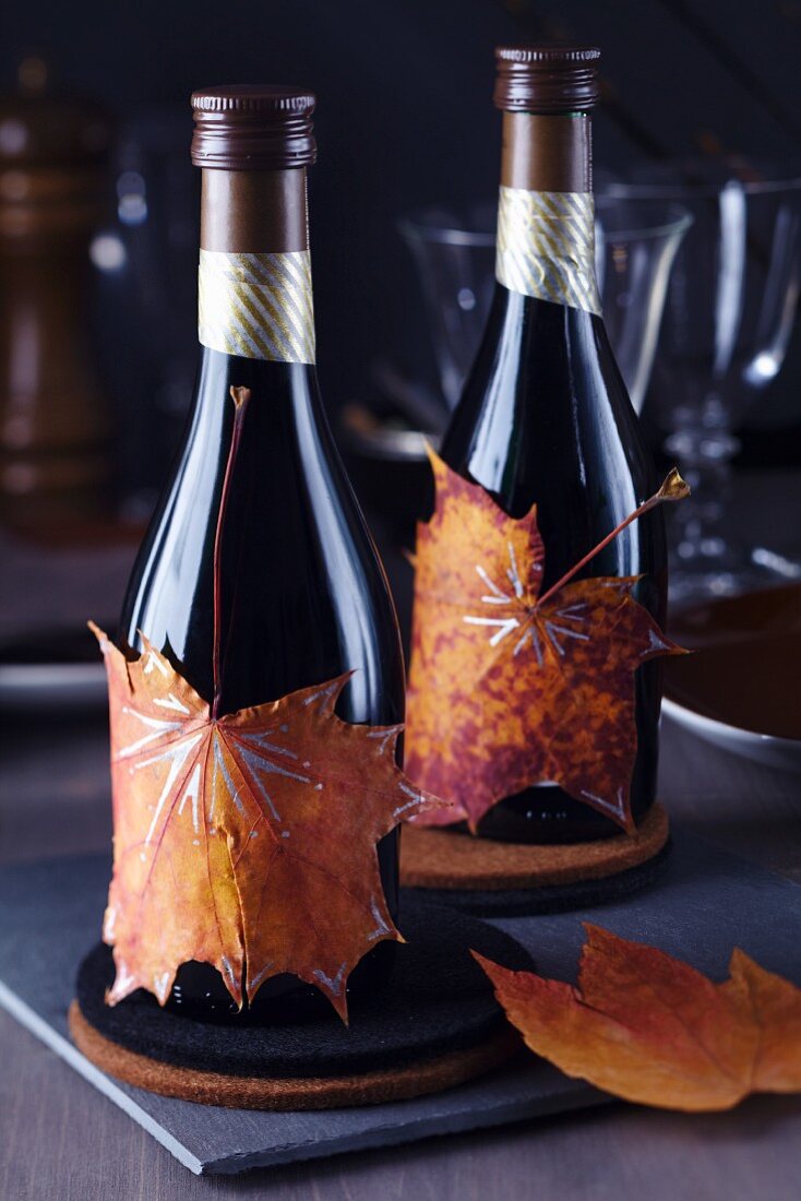 Kleine Weinflaschen beklebt mit bemalten Herbstblättern